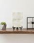 Decorative shelf with a plant, framed picture, and decorative items on a white wall background